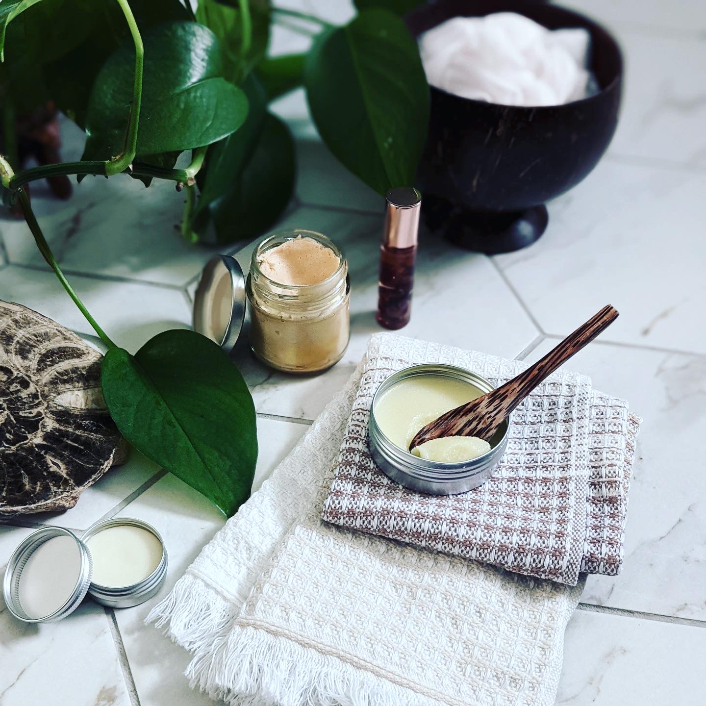 Tubs of cream and skincare products sat on a flannel next to an indoor plant.